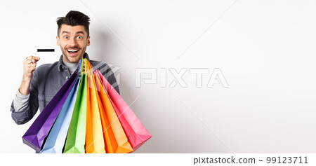 Happy guy shopaholic holding colorful shopping bags and showing plastic credit card, smiling excited, standing white background Happy guy shopaholic holding colorful shopping bags and showing plastic credit card, smiling excited, standing white background 99123711