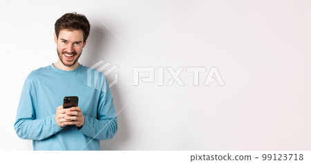 Image of handsome man using smartphone and laughing, smiling at camera joyful, standing over white background Image of handsome man using smartphone and laughing, smiling at camera joyful, standing over white background 99123718