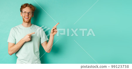 Handsome caucasian man with ginger hair, wearing glasses and t-shirt, pointing fingers right and smiling joyful, showing advertisement, standing over turquoise background 99123738