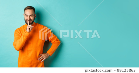 Happy man asking keep voice down, shushing and smiling, prepare surprise, hushing at camera, standing over turquoise background 99123862