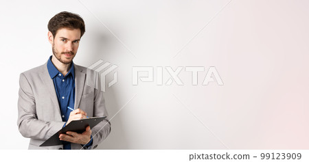 Successful businessman in grey suit taking notes, working in office clothing, holding clipboard and looking at camera, white background 99123909