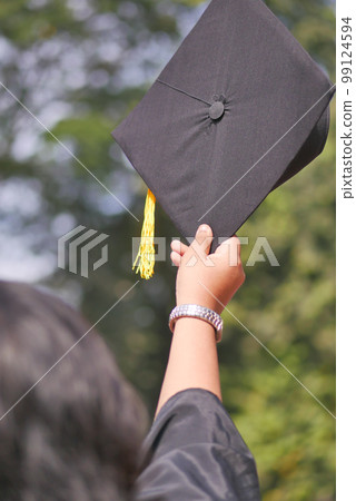 Student hold hats in hand during commencement success on yellow background  99124594
