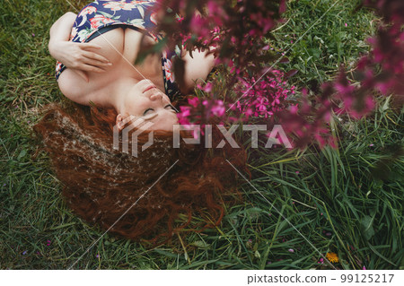 happy redhead young womanlies lies on grass under blossoming pink apple tree happy redhead young womanlies lies on grass under blossoming pink apple tree 99125217