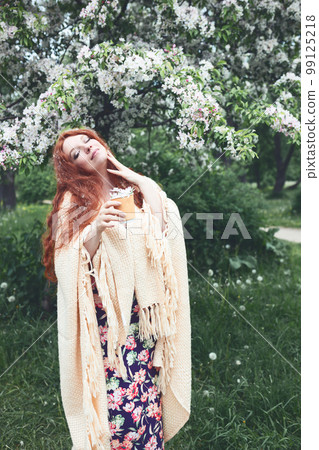 redhead young woman with apple tree flowers in tea paper cup in hands, selective focus redhead young woman with apple tree flowers in tea paper cup in hands, selective focus 99125218
