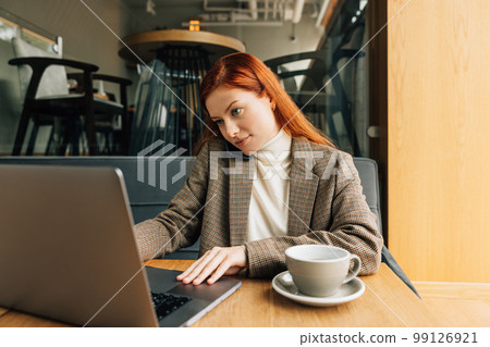 Woman working as a freelancer in a cafe. Female in formal wear typing on laptop and talk on a mobile phone. 99126921