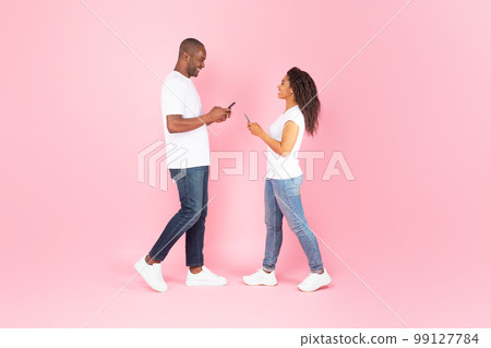 Black middle aged man and young woman using smartphones, standing over pink studio background, full length, side view 99127784