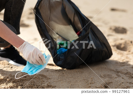 Problem of ocean polution after coronavirus pandemic. Female volunteer picking up trash and medical face masks on beach 99127961