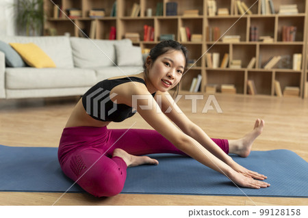 Improve flexibility. Young japanese lady stretching leg and hamstring muscles on yoga mat before domestic workout 99128158