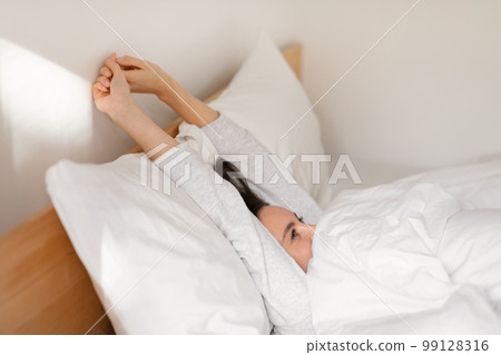 Smiling caucasian millennial lady sleeping on comfortable bed, wake up, stretching body, enjoy softness 99128316