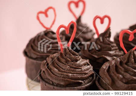 Chocolate cupcakes on a pink background with ganache frosting and red heart chocolate 99129415