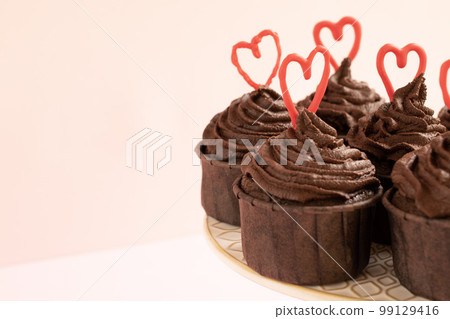 Chocolate cupcakes on a pink background with ganache frosting and red heart chocolate Chocolate cupcakes on a pink background with ganache frosting and red heart chocolate 99129416