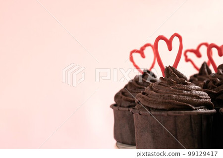 Chocolate cupcakes on a pink background with ganache frosting and red heart chocolate 99129417