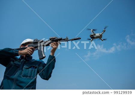 Caucasian man in a helmet shoots a flying drone with a rifle. Caucasian man in a helmet shoots a flying drone with a rifle. 99129939