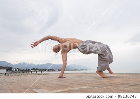Shirtless caucasian man doing backflip on pebble beach.  99130748