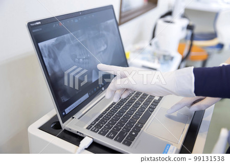Hands of a dental hygienist consulting a treatment policy while looking at an X-ray image at the dentist 99131538