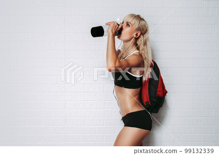 Side view of fit woman with headphones and backpack drink water on white background. Sport Hydration 99132339
