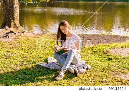 Young hipster girl enjoys sun and nice warm day reading book while relaxing 99133354