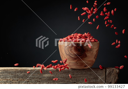 Dried goji berries are poured into a wooden bowl. 99133427