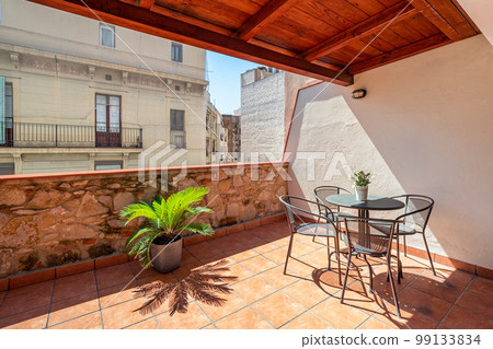 Large terrace with a wooden roof overlooking the city skyline with blue sky. On the terrace flooded with bright sunlight in the middle there is a round table with chairs for a pleasant rest. Large terrace with a wooden roof overlooking the city skyline with blue sky. On the terrace flooded with bright sunlight in the middle there is a round table with chairs for a pleasant rest. 99133834