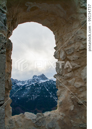 Fuessen, Germany - January 14th 2023 - Looking through a window of the Falkenstein ruin towards the Alps Fuessen, Germany - January 14th 2023 - Looking through a window of the Falkenstein ruin towards the Alps 99134737