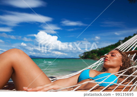 Woman laying in hammock on beach 99135695