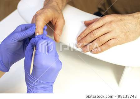 Cropped male hands on workstation in manicure beauty salon. Nail professional doing mature man nail treatment in spa, pushing cuticle back with orange stick. Safe eco Japanese manicure. Horizontal Cropped male hands on workstation in manicure beauty salon. Nail professional doing mature man nail treatment in spa, pushing cuticle back with orange stick. Safe eco Japanese manicure. Horizontal 99135748