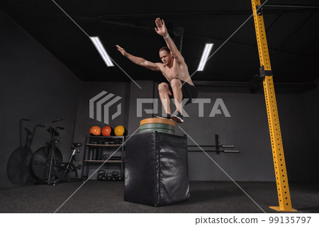 Crossfit athlete doing box jumping exercise at gym 99135797