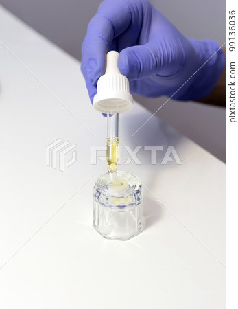 Closeup Nail technician holds pipette with natural oil for cuticle, fingernails above glass cup. Eco Japanese bio manicure. Safe nail treatment for adults, children, expectant moms.Vertical plane Closeup Nail technician holds pipette with natural oil for cuticle, fingernails above glass cup. Eco Japanese bio manicure. Safe nail treatment for adults, children, expectant moms.Vertical plane 99136036