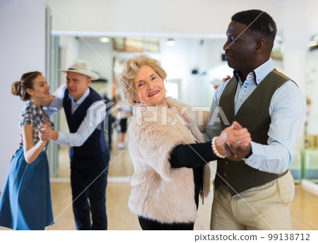 Elderly woman learning ballroom dancing in pair in dance studio Elderly woman learning ballroom dancing in pair in dance studio 99138712