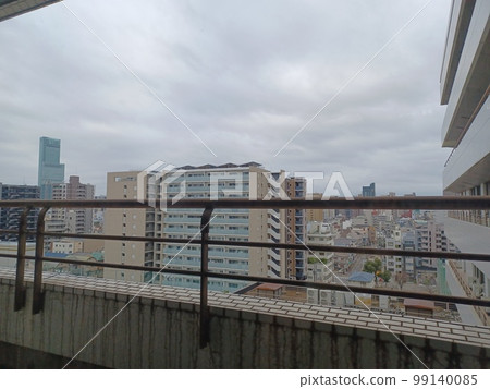 A desolate cityscape seen through the rusted red-brown railing of a balcony against a cloudy sky 99140085