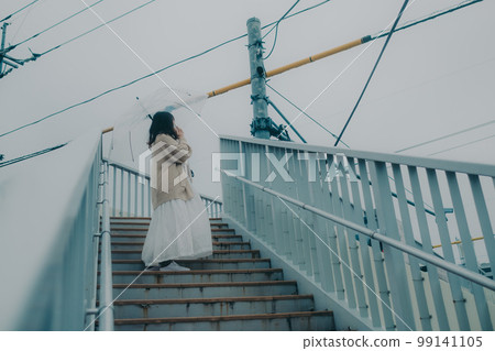Photo of a woman holding an umbrella on an overpass and holding a smartphone 99141105