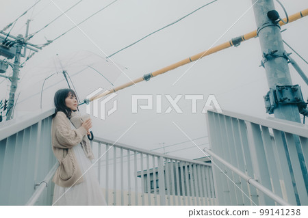 Photo of a woman holding an umbrella on an overpass and drinking coffee while waiting for a meeting 99141238