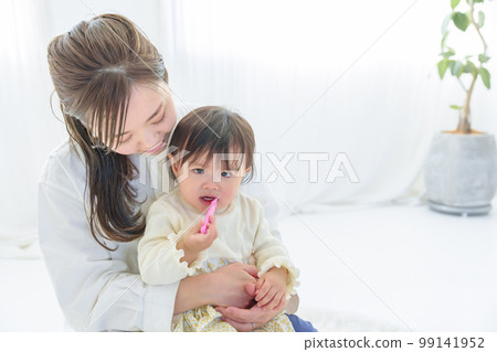 baby brushing teeth on mom's lap 99141952