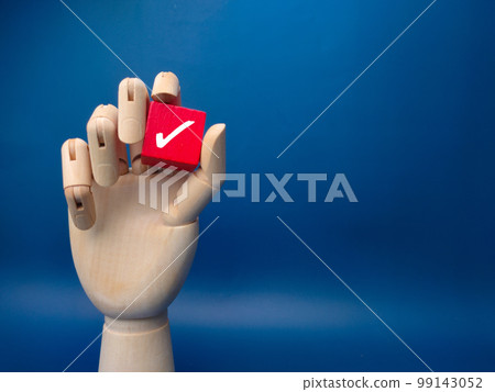 Wooden hand holding red cube with correct sign on blue background. Business concept. Wooden hand holding red cube with correct sign on blue background. Business concept. 99143052