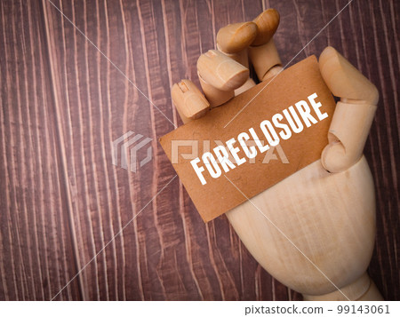 Wooden hand holding card board with the word FORECLOSURE. Wooden hand holding card board with the word FORECLOSURE. 99143061