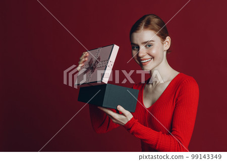 Red hair woman open to pink gift box with ribbon. Studio shot portrait 99143349