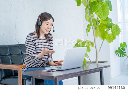 Woman working from home with headset and video chatting Woman working from home with headset and video chatting 99144180