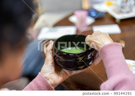 一位在餐桌上製作和飲用稀薄綠茶（綠茶）的老婦人的手 99144191