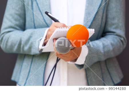 Female reporter at press conference, writing notes, holding microphone 99144280
