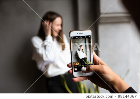 Two young women take photos and videos of each other on smartphone on a terrace Two young women take photos and videos of each other on smartphone on a terrace 99144367