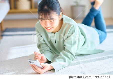 Smiling young woman operating a smartphone in a bright room Smiling young woman operating a smartphone in a bright room 99144531