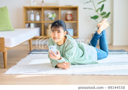 Smiling young woman operating a smartphone in a bright room Smiling young woman operating a smartphone in a bright room 99144538