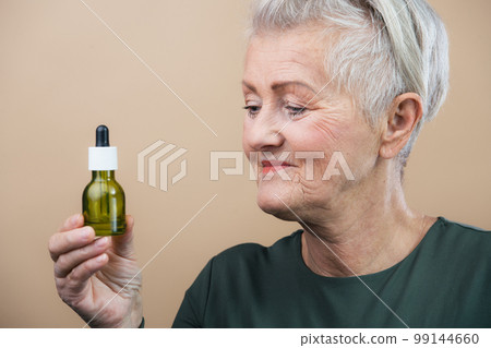 Portrait of smiling senior woman holding skincare serum drops in studio.Concept of beauty and skincare. 99144660