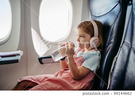 Little girl in airplane drinking water and listening music. 99144662
