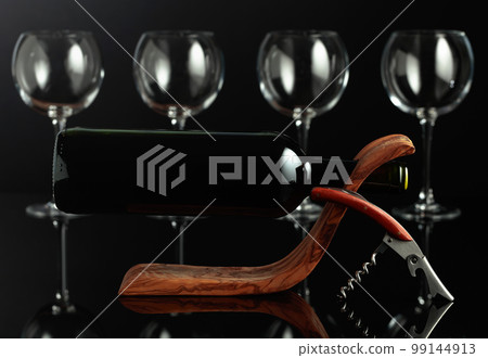Bottle of red wine in a wooden bottle holder and empty glasses. Bottle of red wine in a wooden bottle holder and empty glasses. 99144913