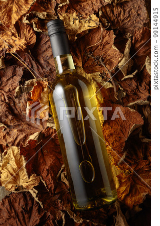 Bottle of white wine on the dried-up vine leaves. Bottle of white wine on the dried-up vine leaves. 99144915