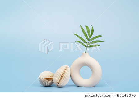 Easter concept. Ivory vase with palm leaf and two paper craft Easter eggs on blue background monochrome 99145070