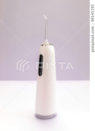 Oral teeth irrigator with nozzle pack, dental water tooth cleaner, white portable rechargeable cordless water dental flosser on purple background. Waterproof home dental care device. Vertical Oral teeth irrigator with nozzle pack, dental water tooth cleaner, white portable rechargeable cordless water dental flosser on purple background. Waterproof home dental care device. Vertical 99145195