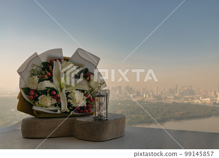 Hourglass or Sandglass is next to Bouquet of flowers placed on the timber outside the balcony. Hourglass or Sandglass is next to Bouquet of flowers placed on the timber outside the balcony. 99145857