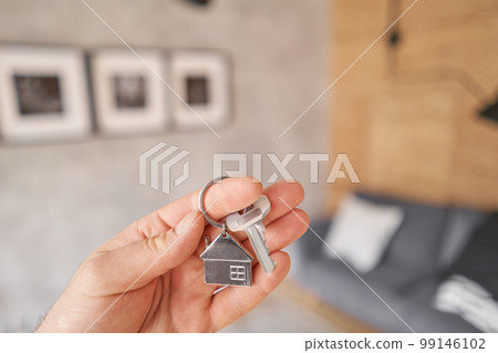 Men hand holding key with house shaped keychain. Modern light lobby interior. Mortgage concept. Real estate, moving home or renting property. Men hand holding key with house shaped keychain. Modern light lobby interior. Mortgage concept. Real estate, moving home or renting property. 99146102